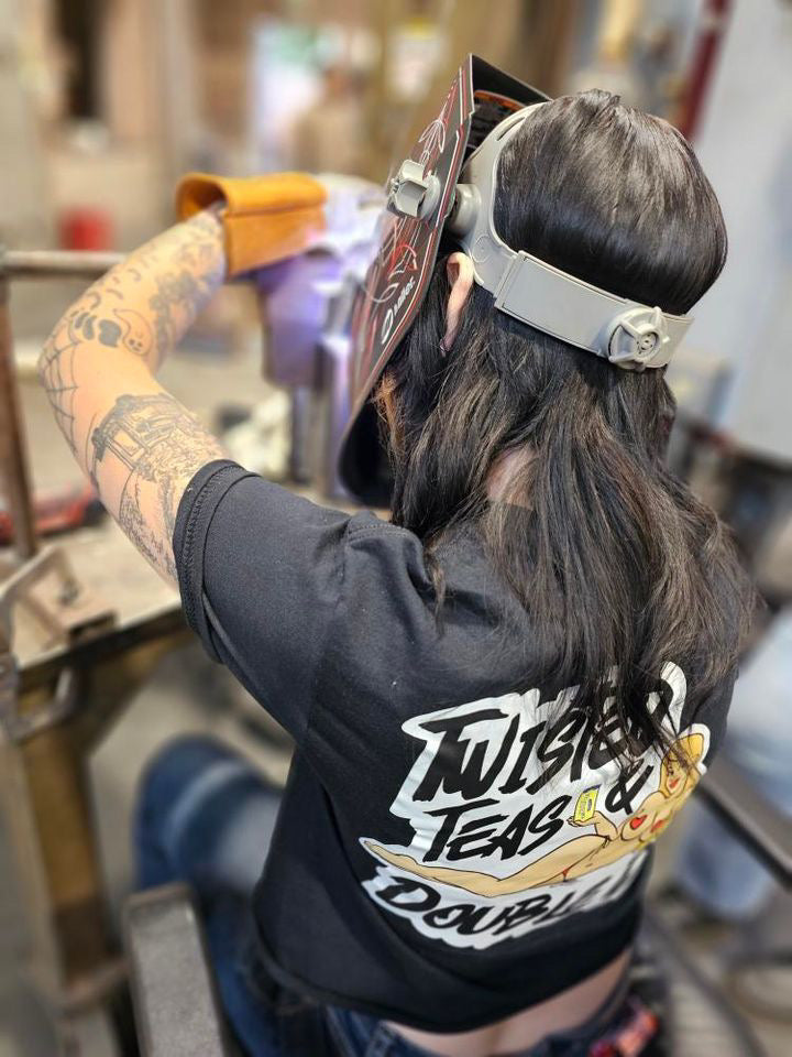 Person wearing a black shirt with graphic design, sitting in a chair welding.
